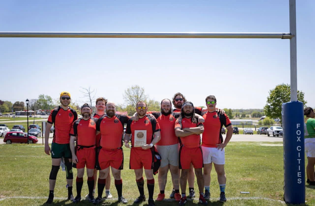 Escanaba Berserkers side lined up under the posts with a tournament plaque, red kits.